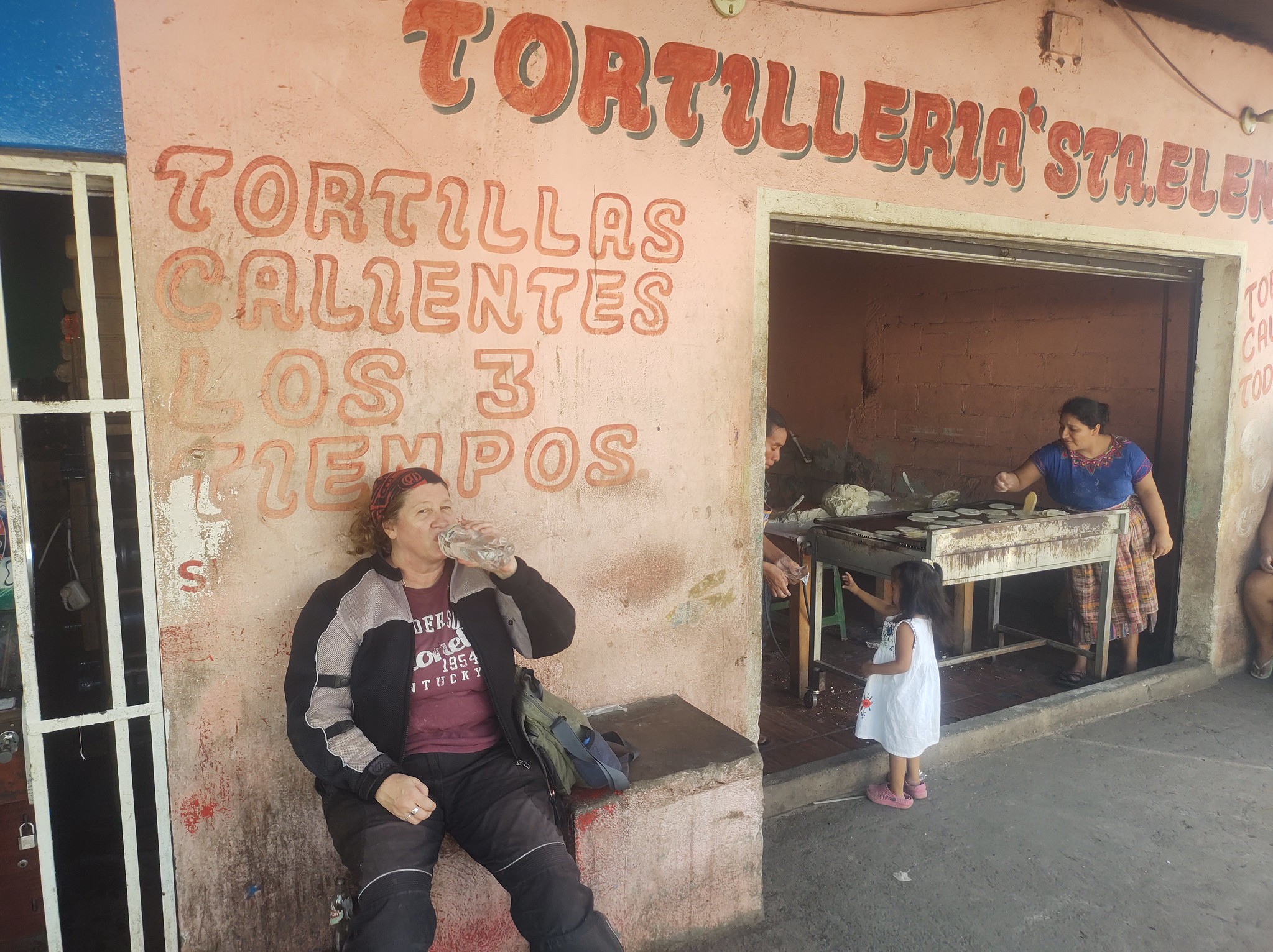 a woman in motorcycle gear sits on a
        bench drinking water