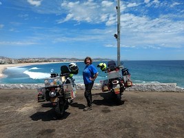 motorcycle rider standing between two motorcycles with an ocean in the background
